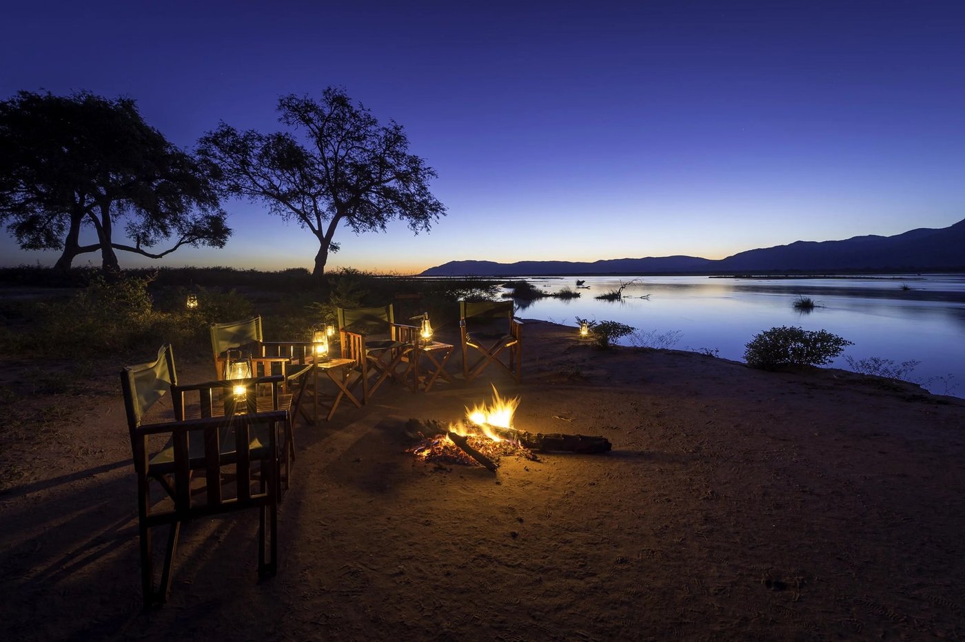 Riverside dining deck lit by a fire pit at night at John's Camp.