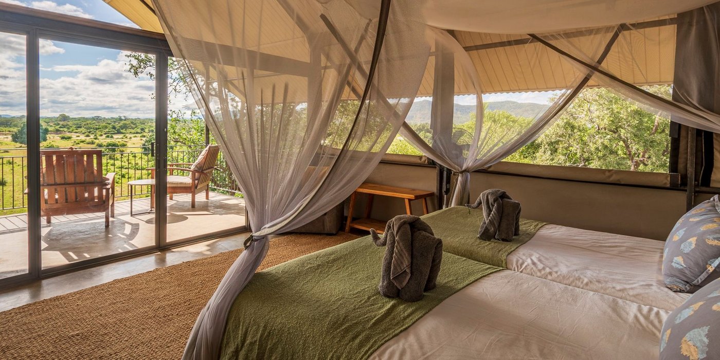 Bedroom with a draped mosquito net and a floodplain view at Kavinga Safari Camp.