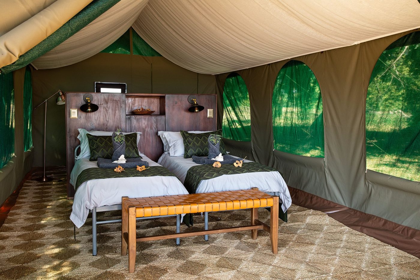 Twin bedroom with patterned bedding and wooden bench at Mana River Camp.