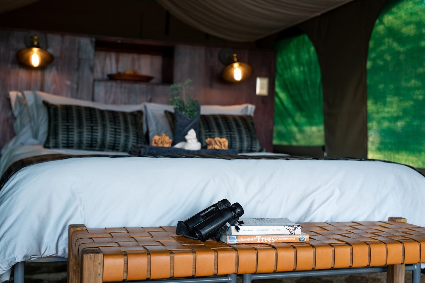 Bedroom with a leather bench and binoculars laid out at Mana River Camp.
