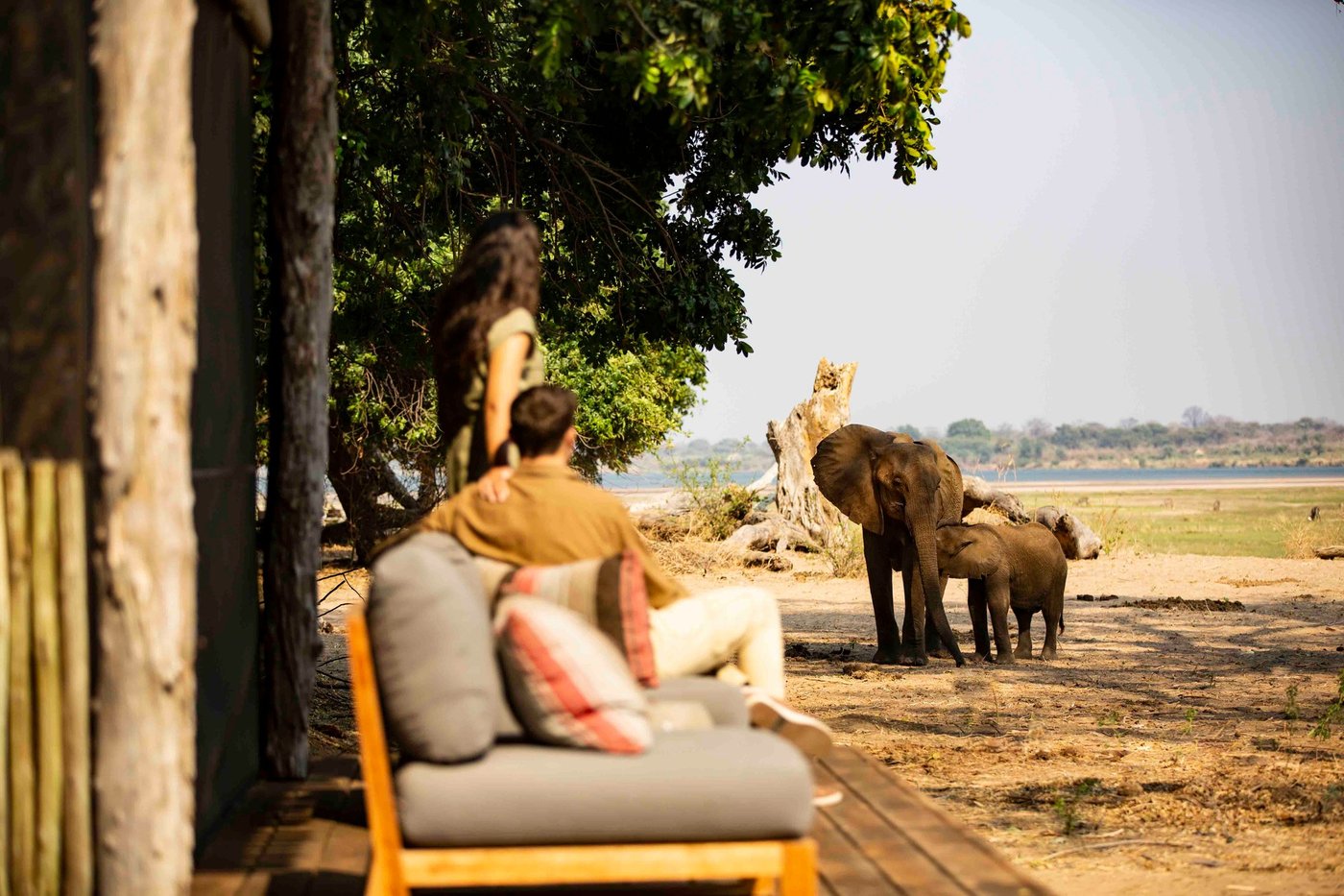 Canvas lounge chairs on a deck as elephants pass close by at Wilderness Little Ruckomechi.