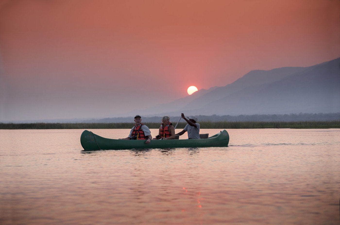 Canoe safari gliding across the Zambezi at sunset from Zambezi Expeditions.